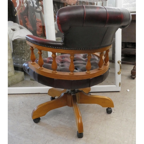 53 - A modern stained beech framed swivel office chair, upholstered in faux maroon hide, on casters