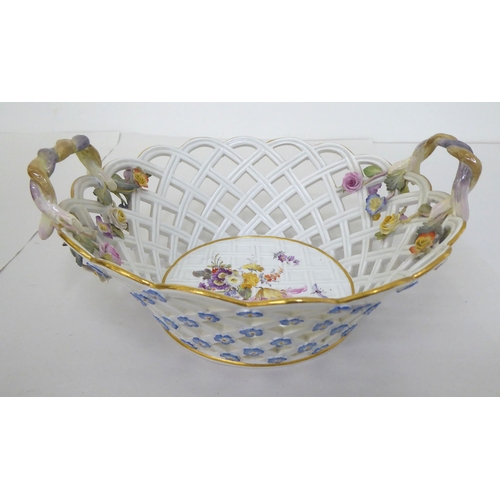 60 - A Meissen porcelain centrepiece fruit bowl with twin handles, over a latticeworked design basket, de... 