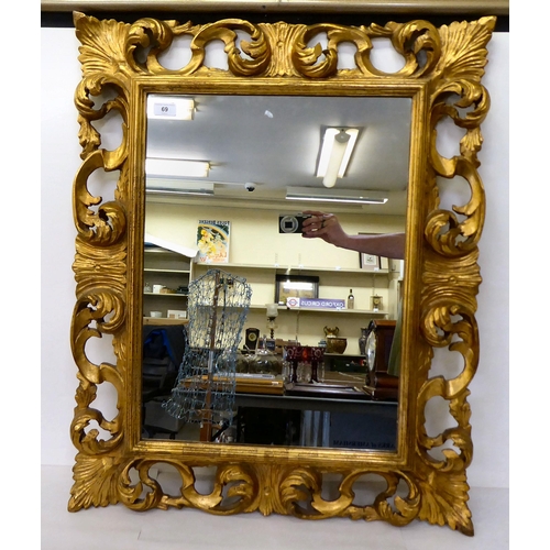 69 - A 19thC style mirror, set in a boldly scrolled and carved giltwood frame  33