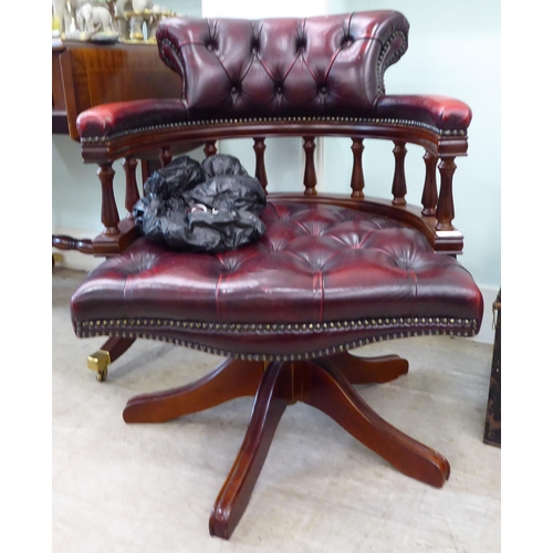 105 - A modern horseshoe shape desk chair, upholstered in buttoned, burnished maroon hide, pivoting on a q... 