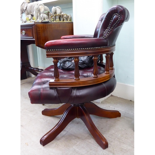 105 - A modern horseshoe shape desk chair, upholstered in buttoned, burnished maroon hide, pivoting on a q... 