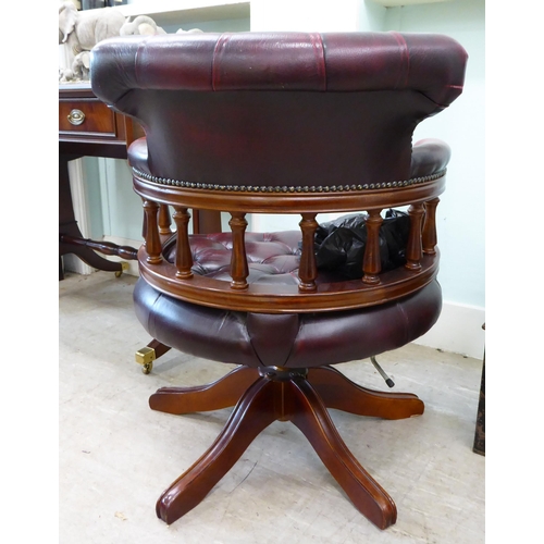 105 - A modern horseshoe shape desk chair, upholstered in buttoned, burnished maroon hide, pivoting on a q... 