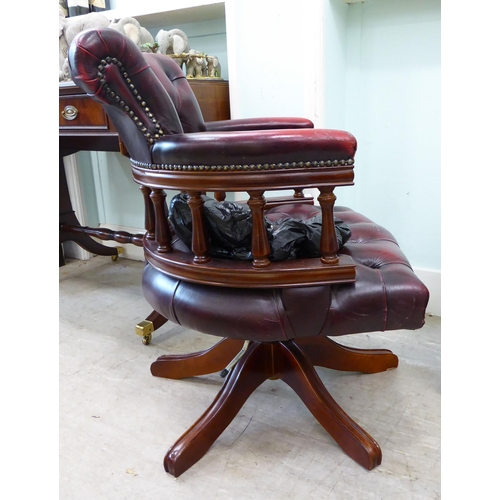 105 - A modern horseshoe shape desk chair, upholstered in buttoned, burnished maroon hide, pivoting on a q... 