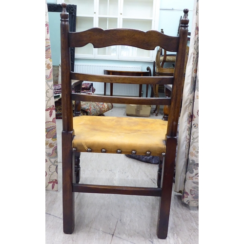 110 - A 19thC style stained beech framed, low, open arm, ladder back chair with a studded and aged, hide u... 