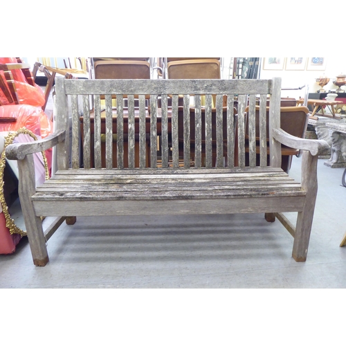 288 - A weathered, slatted teak garden bench, raised on square legs  60