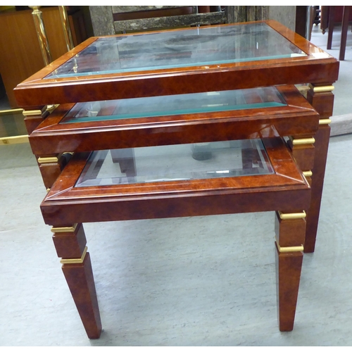 323 - A modern nesting set of three walnut finished occasional tables, each with a glass top, raised on sq... 