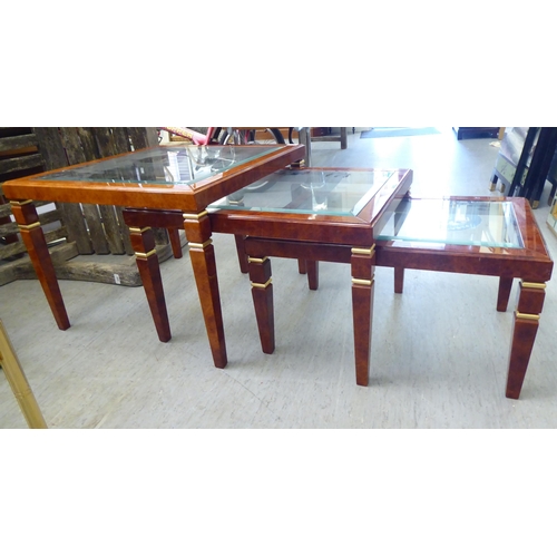 323 - A modern nesting set of three walnut finished occasional tables, each with a glass top, raised on sq... 