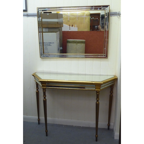 331 - A modern gilded console table with a mirrored top, raised on turned, tapered legs; and a matching mi... 