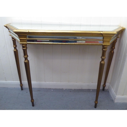 331 - A modern gilded console table with a mirrored top, raised on turned, tapered legs; and a matching mi... 