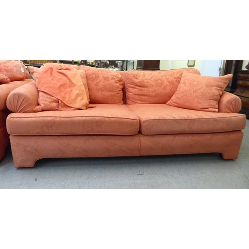 129 - A modern two person settee with a level, low back and scrolled arms, upholstered in burnt orange col... 