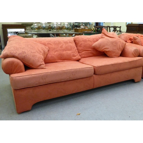 130 - A modern two person settee with a level, low back and scrolled arms, upholstered in burnt orange col... 