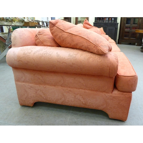 130 - A modern two person settee with a level, low back and scrolled arms, upholstered in burnt orange col... 