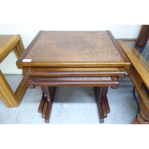 151 - A (probably G-Plan) nesting set of three teak framed tables, the tops set with a spot-hammered coppe... 