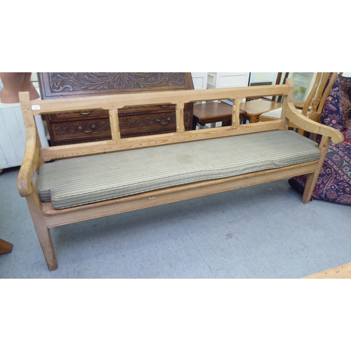 273 - A modern pine bench, the canted bar back and open arms enclosing a cushioned seat, raised on tapered... 