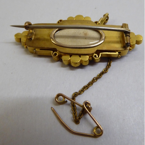 7 - A late Victorian yellow metal mourning brooch with enamelled decoration, set with seed pearls