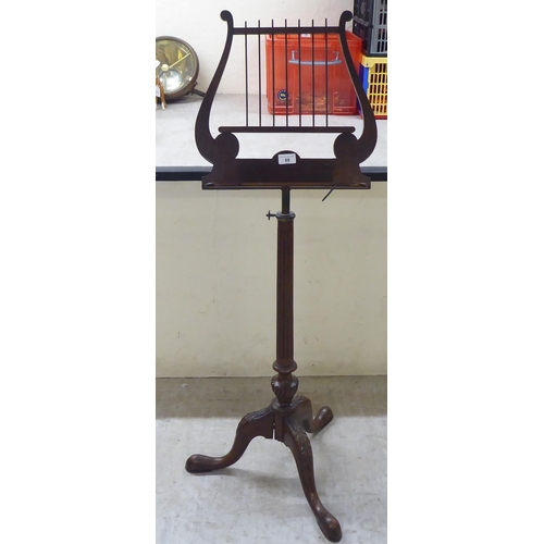 88 - An early/mid 20thC mahogany music stand with a lyre shaped top, over a fluted column and tripod base... 