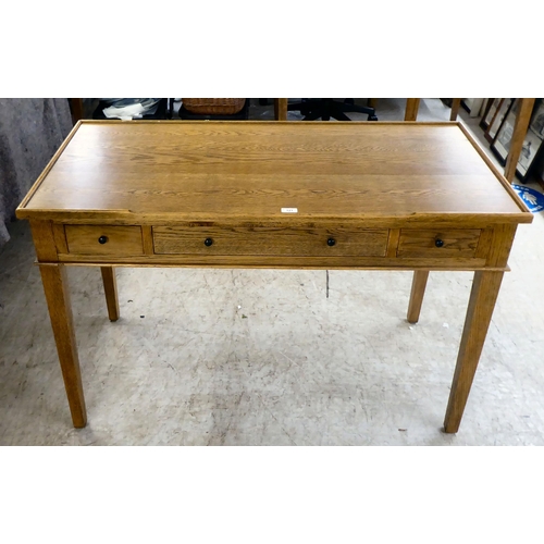 121 - A modern OKA oak desk with three drawers, raised on square, tapered legs  31