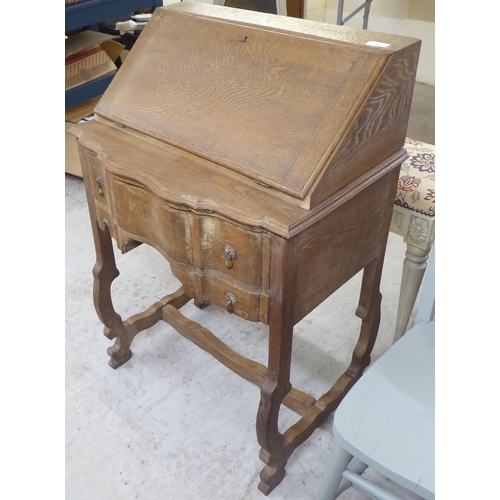 36 - A 1930s limed oak bureau with a fall flap and two drawers, raised on curved legs  37