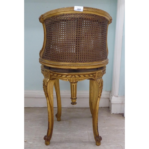 302 - A late 19thC French giltwood, revolving dressing table chair with a caned back and seat, raised on c... 