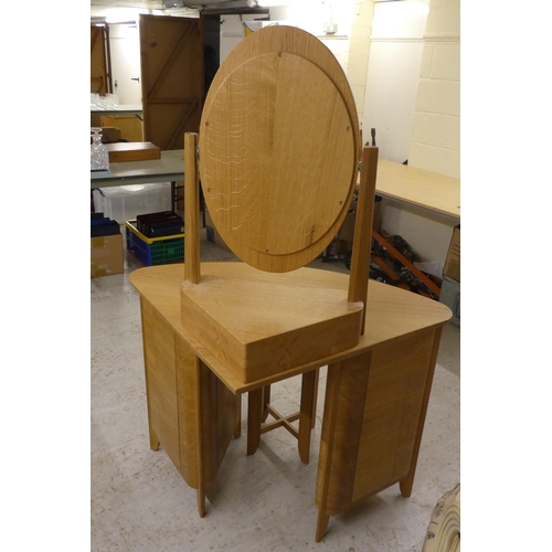 77 - A modern light oak dressing table, surmounted by an oval mirror and single drawer base, over two ped... 