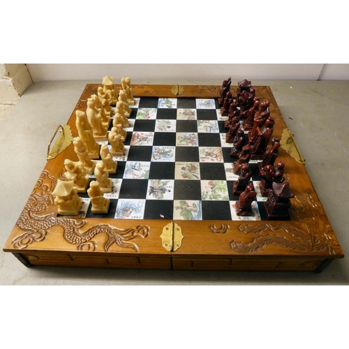 204 - A Oriental style resin chess set, in a fold-out board carrying case, set dragon carved carrying case... 