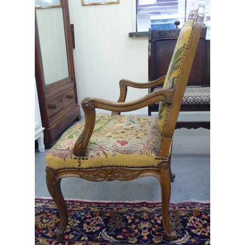 34 - An overpainted open arm library chair, the back and seat cushions tapestry upholstered, raised on ca... 