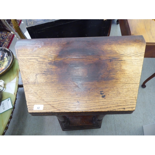 42 - A mid 20thC Gothic design oak side table with a hinged top, over a carved, panelled front, raised on... 