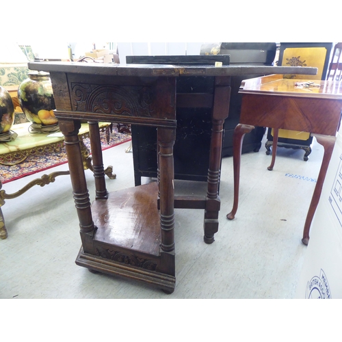 42 - A mid 20thC Gothic design oak side table with a hinged top, over a carved, panelled front, raised on... 