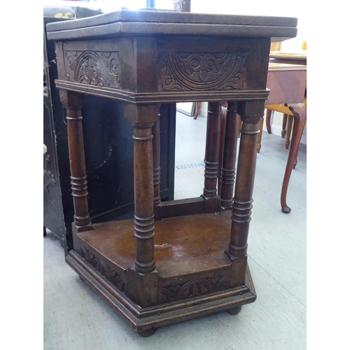 42 - A mid 20thC Gothic design oak side table with a hinged top, over a carved, panelled front, raised on... 