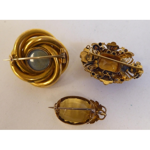 91 - Three yellow metal brooches: to include one set with a central yellow stone, surrounded by floral fi... 