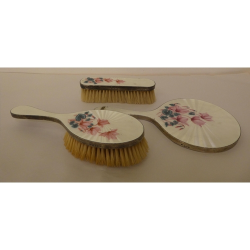 297 - A three piece silver backed dressing table set with engine turned, floral decorated enamel ornament&... 