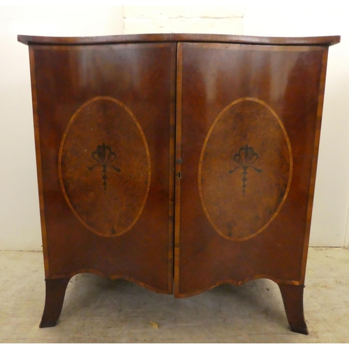 37 - An Edwardian crossbanded yew and mahogany serpentine front, two door cabinet, enclosing two open she... 