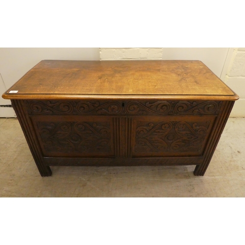 49 - A late 18thC oak chest with a hinged lid, over a double panelled front with scroll carved ornament, ... 