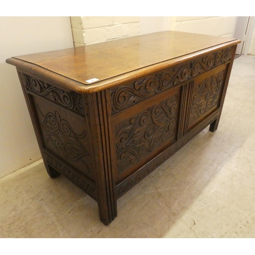 49 - A late 18thC oak chest with a hinged lid, over a double panelled front with scroll carved ornament, ... 