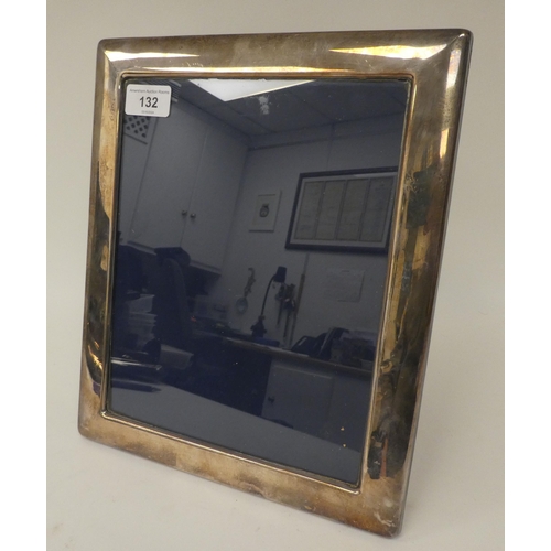 132 - A silver photograph frame, in a plain surround with a glazed aperture, on a fabric back and easel st... 