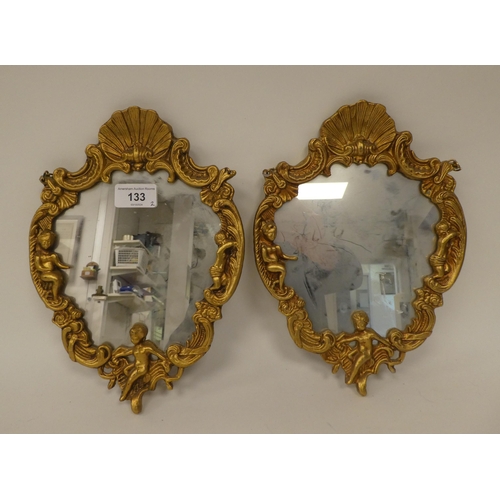 133 - A pair of modern mirrors, set in elaborately, scroll, shell and cherubic figure moulded gilt frames&... 