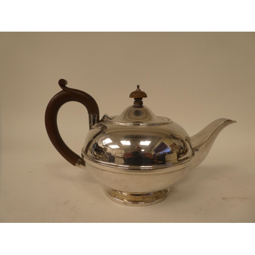 234 - A silver teapot of squat, bulbous form with a swept spout, hinged lid, insulated handle and knop, on... 