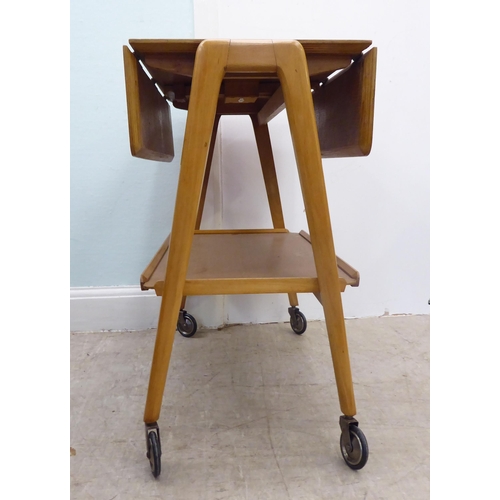 98 - A circa 1950-70s Remploy light oak drop-leaf, two tier hostess trolley, raised on straight legs and ... 