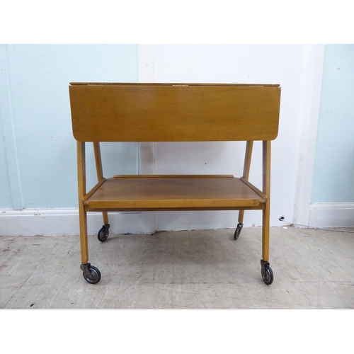 98 - A circa 1950-70s Remploy light oak drop-leaf, two tier hostess trolley, raised on straight legs and ... 