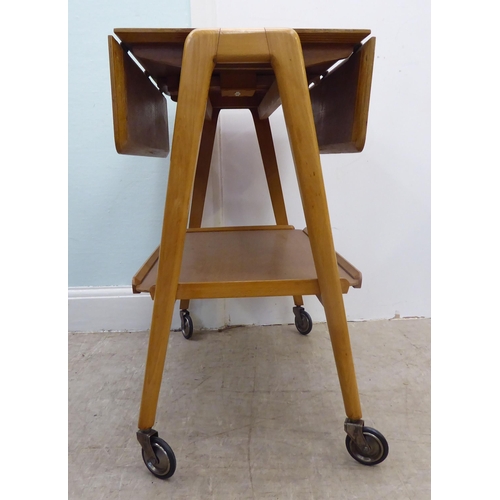 98 - A circa 1950-70s Remploy light oak drop-leaf, two tier hostess trolley, raised on straight legs and ... 