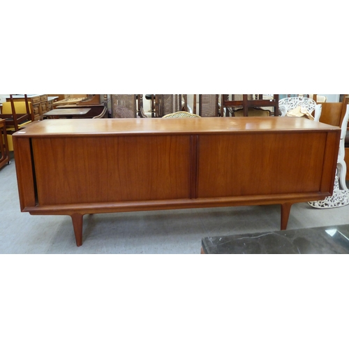 355 - A 1960/70s teak sideboard with two tambour sliding doors, enclosing a shelved interior, raised on tu... 