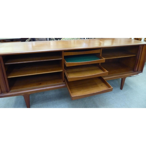 355 - A 1960/70s teak sideboard with two tambour sliding doors, enclosing a shelved interior, raised on tu... 