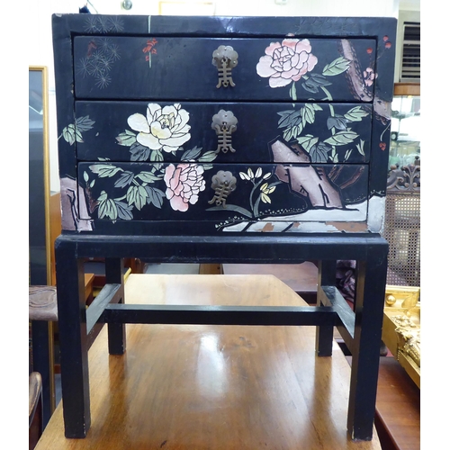 357 - A modern Chinese inspired black lacquered and overpainted, three drawer bedside chest, raised on blo... 