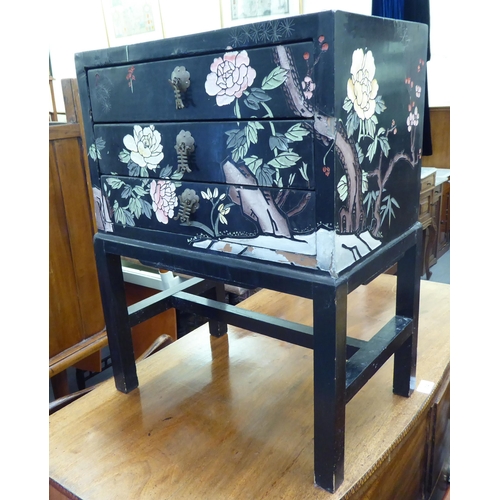 357 - A modern Chinese inspired black lacquered and overpainted, three drawer bedside chest, raised on blo... 