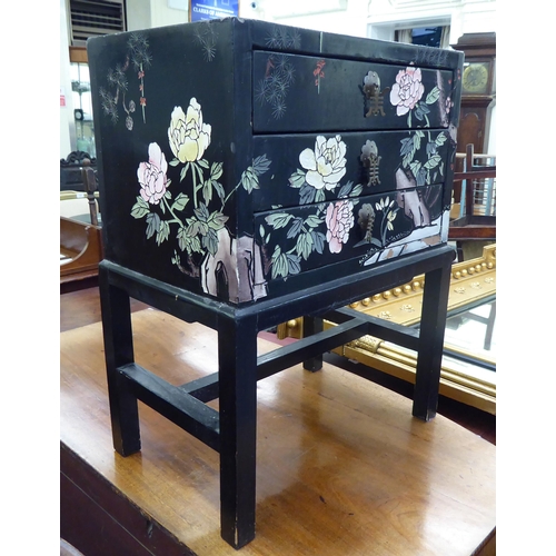 357 - A modern Chinese inspired black lacquered and overpainted, three drawer bedside chest, raised on blo... 