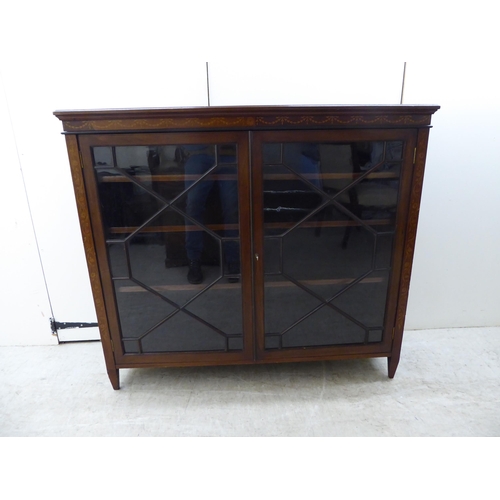 133 - An Edwardian string inlaid and marquetry mahogany, two door glazed bookcase, raised on tapered legs ... 