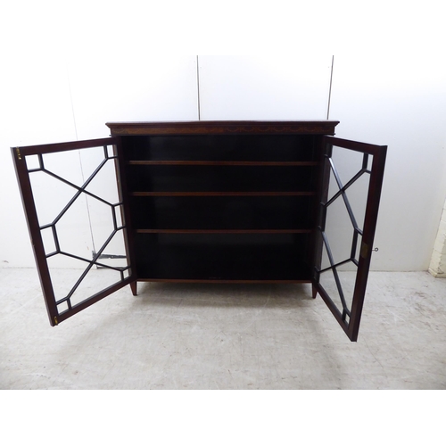 133 - An Edwardian string inlaid and marquetry mahogany, two door glazed bookcase, raised on tapered legs ... 