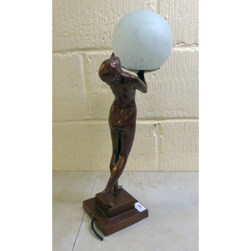 143 - A modern reproduction of an Art Deco inspired bronze table lamp, fashioned as a nude, holding a sphe... 