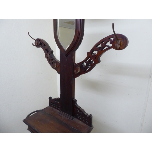 94 - A 1920s oak hallway hat/stickstand with a shield shaped mirror, eight hooks and a hinged compartment... 