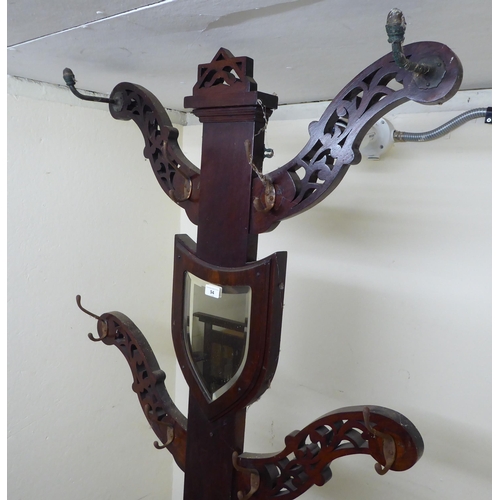 94 - A 1920s oak hallway hat/stickstand with a shield shaped mirror, eight hooks and a hinged compartment... 